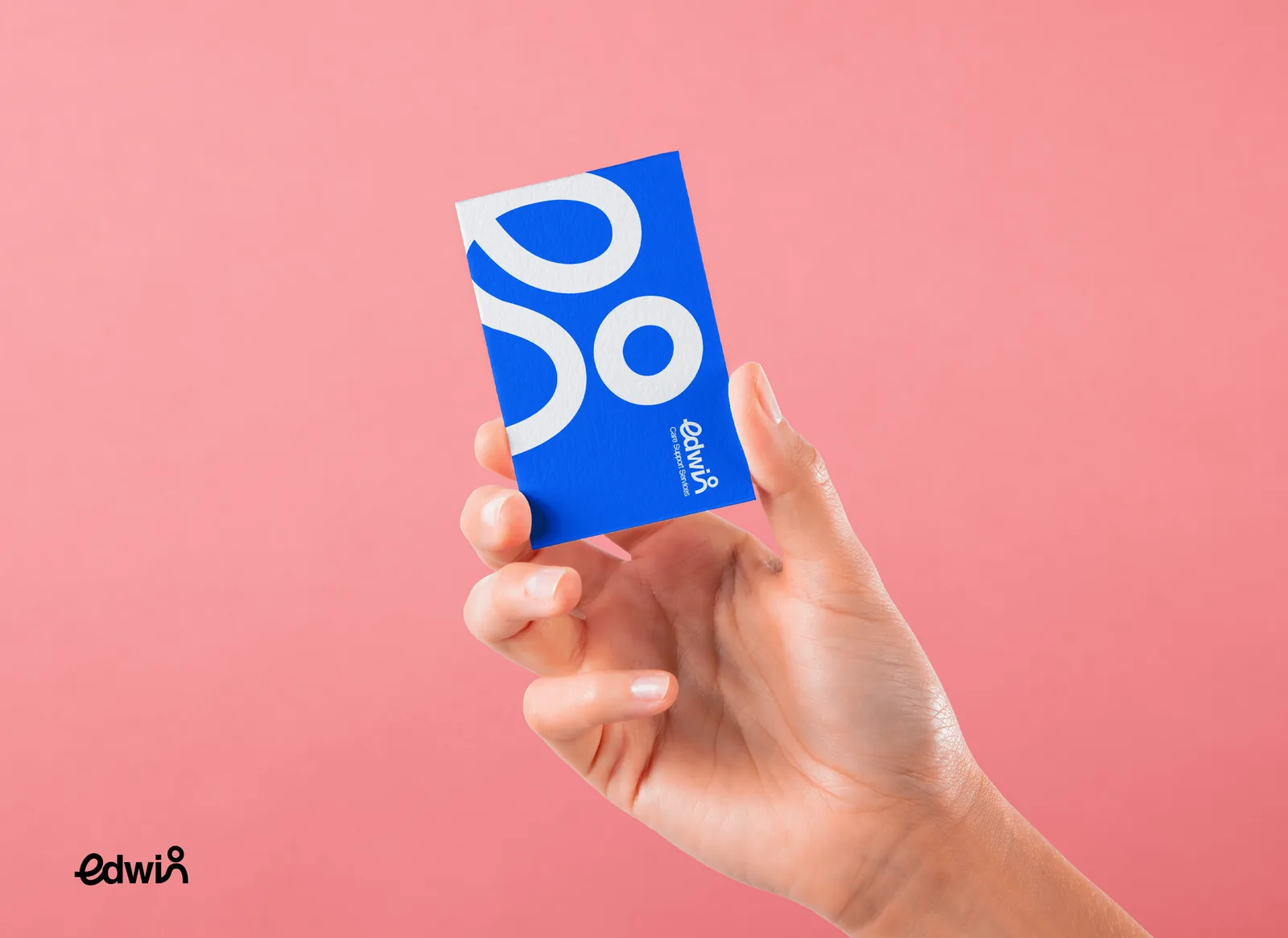 Hand holding a blue Edwin business card printed with the white figure motif, on a pink background