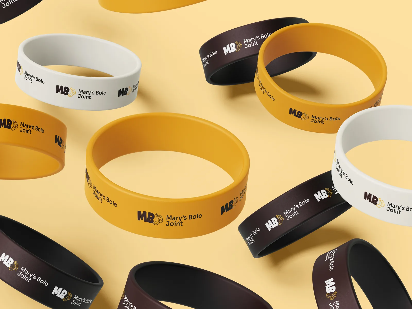 Mary's Bole Joint silicone wristbands in chocolate, golden yellow and cream scattered on a butter-yellow surface